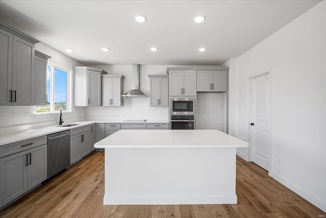 kitchen with wall chimney exhaust hood, a sink, stainless steel appliances, gray cabinets, and a kitchen island