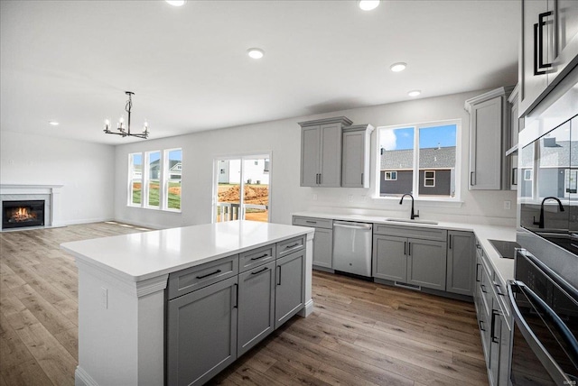 kitchen featuring stainless steel dishwasher, wall oven, gray cabinets, wood finished floors, and a sink