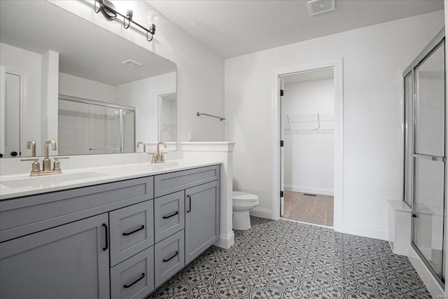 bathroom with double vanity, a shower stall, a walk in closet, visible vents, and a sink