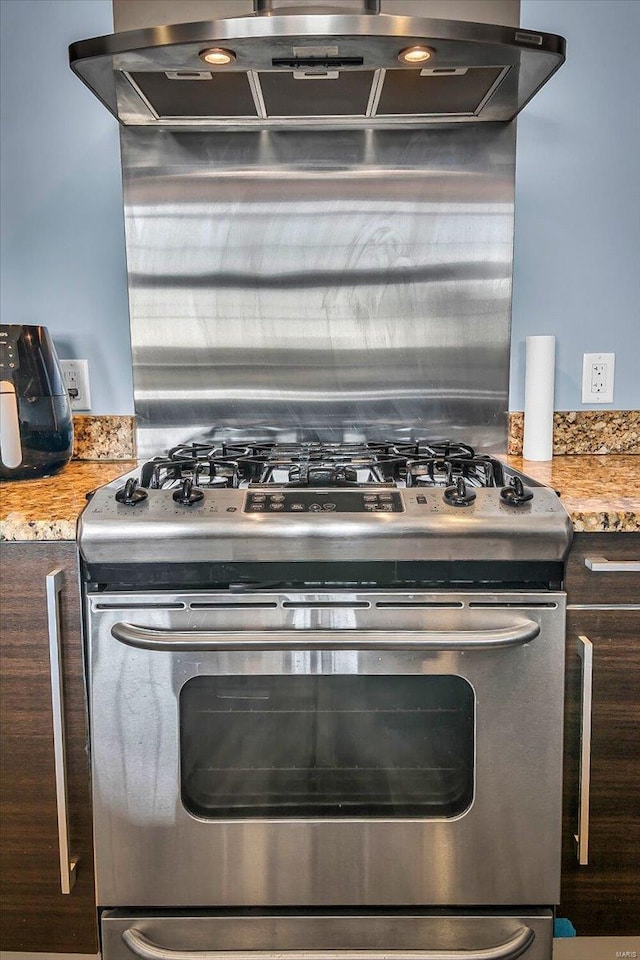 kitchen with gas range, range hood, light stone counters, and dark brown cabinets