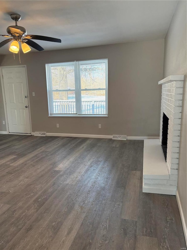 unfurnished living room with ceiling fan, dark wood-type flooring, and a brick fireplace