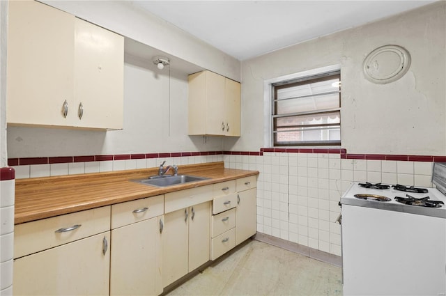 kitchen featuring sink, tile walls, white range with gas cooktop, and cream cabinetry