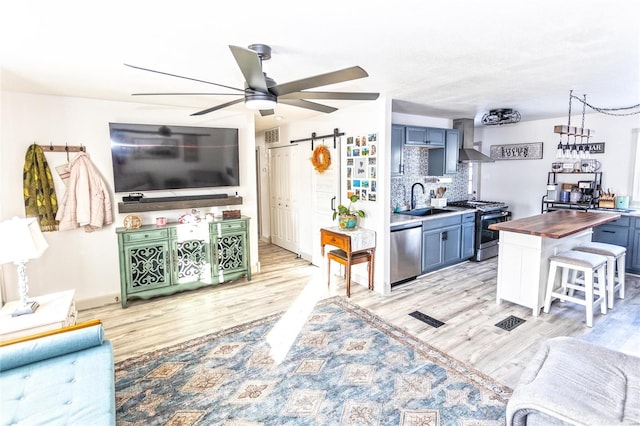 kitchen with a barn door, stainless steel appliances, a kitchen bar, wall chimney range hood, and butcher block counters