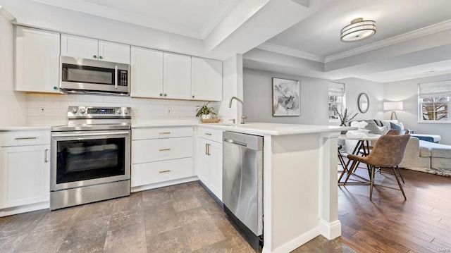 kitchen featuring kitchen peninsula, stainless steel appliances, white cabinets, and tasteful backsplash