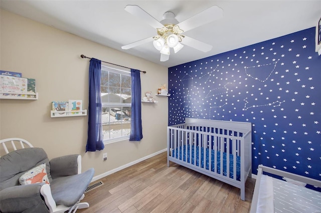 bedroom with a nursery area, ceiling fan, and hardwood / wood-style flooring