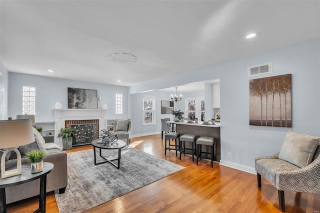 living room with light hardwood / wood-style floors, an inviting chandelier, and a fireplace