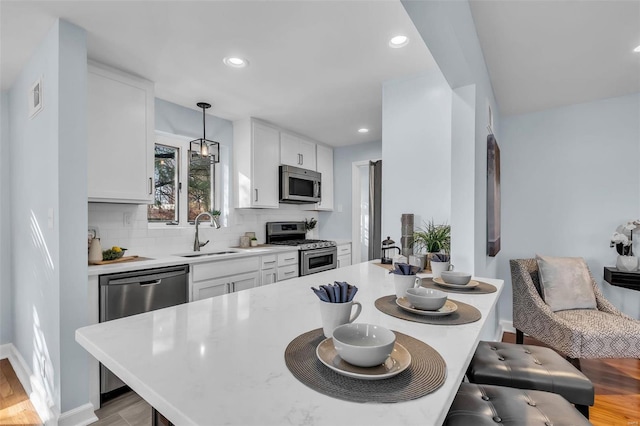 kitchen featuring appliances with stainless steel finishes, pendant lighting, white cabinets, backsplash, and sink