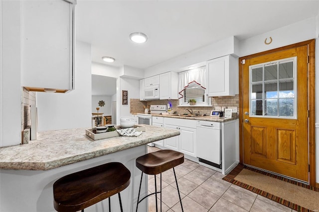 kitchen with white appliances, a kitchen bar, white cabinets, sink, and light tile patterned flooring