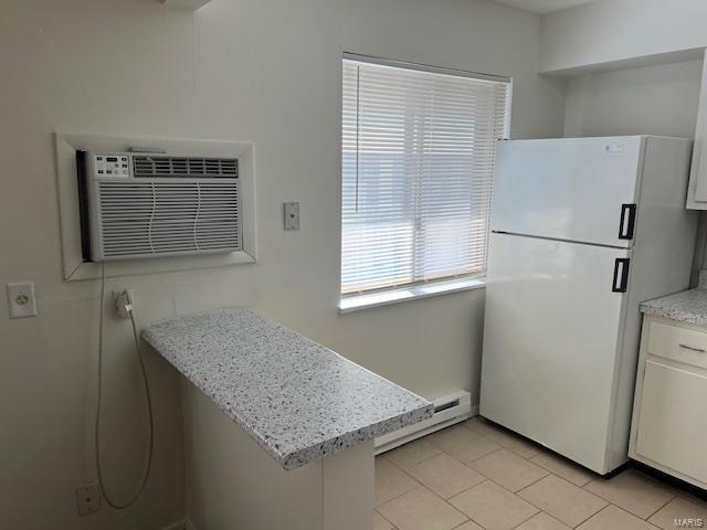 kitchen featuring white refrigerator, white cabinets, a baseboard heating unit, light stone countertops, and a wall unit AC