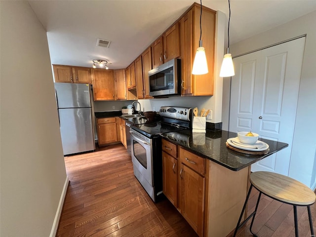 kitchen featuring dark wood-type flooring, dark stone counters, hanging light fixtures, a breakfast bar area, and stainless steel appliances