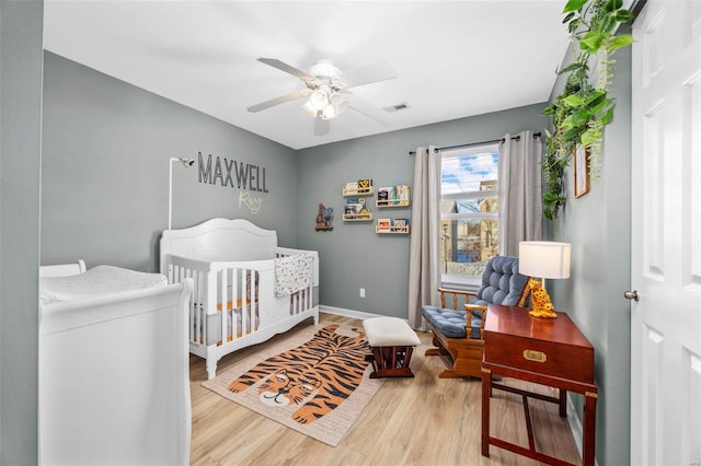 bedroom with a nursery area, light wood-type flooring, and ceiling fan