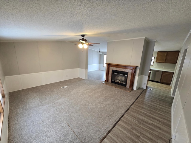 unfurnished living room featuring a fireplace, a textured ceiling, ceiling fan, and dark wood-type flooring