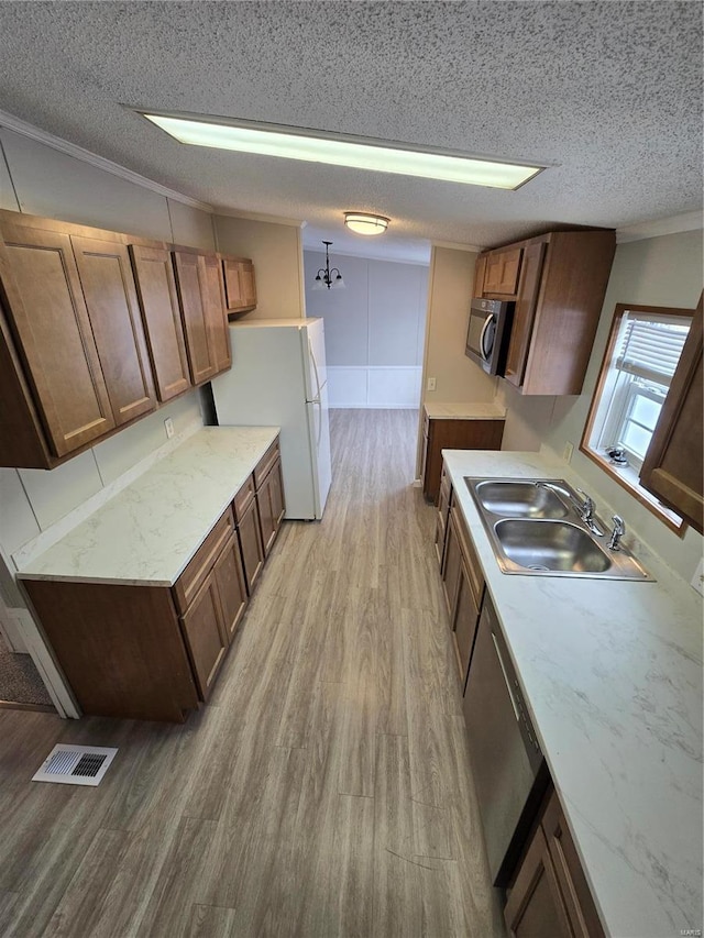 kitchen featuring light wood-type flooring, ornamental molding, a textured ceiling, stainless steel appliances, and sink