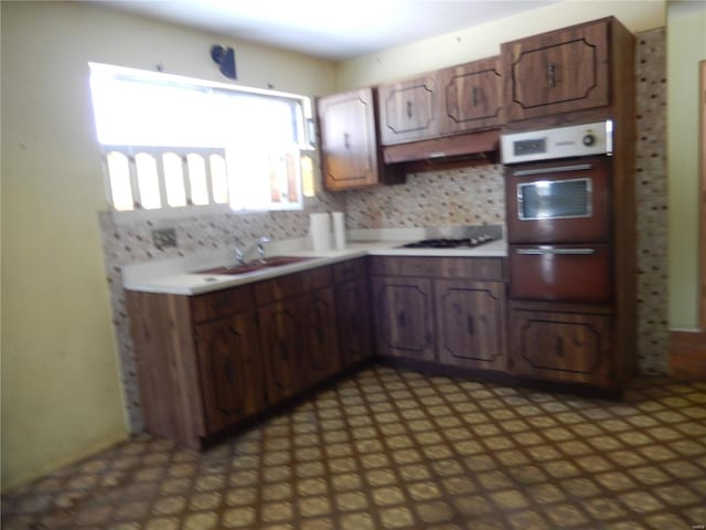 kitchen with wall oven, backsplash, dark brown cabinets, white gas cooktop, and sink