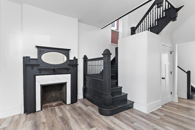 staircase featuring a high end fireplace, baseboards, and wood finished floors