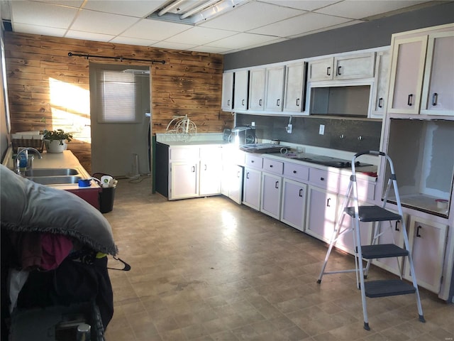 kitchen featuring a drop ceiling, white cabinets, wood walls, and sink