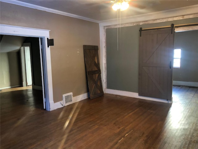 spare room featuring ceiling fan, dark hardwood / wood-style floors, ornamental molding, and a barn door