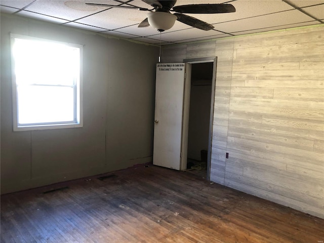 unfurnished room featuring dark wood-type flooring, a paneled ceiling, wooden walls, and ceiling fan