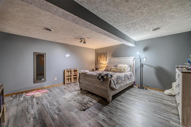 bedroom featuring beam ceiling, light wood-type flooring, and a textured ceiling