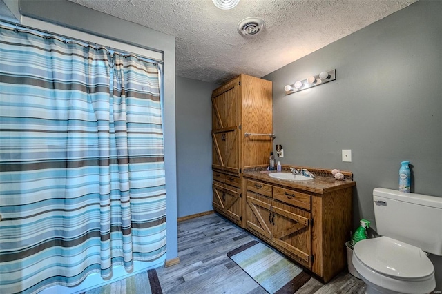 bathroom featuring a shower with shower curtain, vanity, a textured ceiling, hardwood / wood-style flooring, and toilet