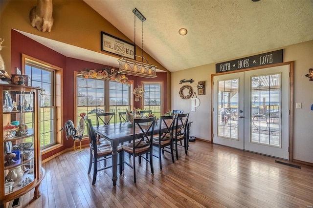 dining space featuring french doors, a textured ceiling, vaulted ceiling, and hardwood / wood-style floors