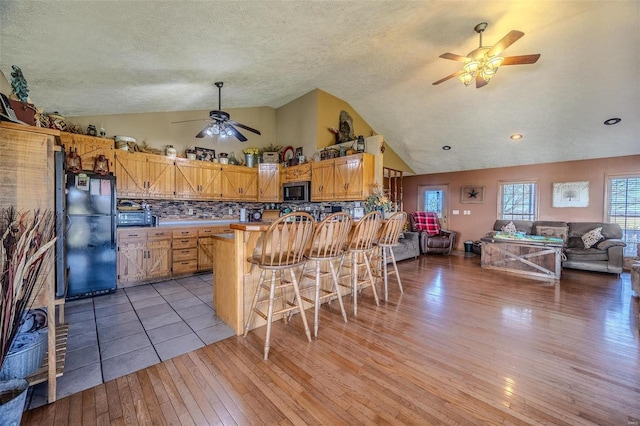 kitchen with black fridge, lofted ceiling, a kitchen bar, decorative backsplash, and light wood-type flooring