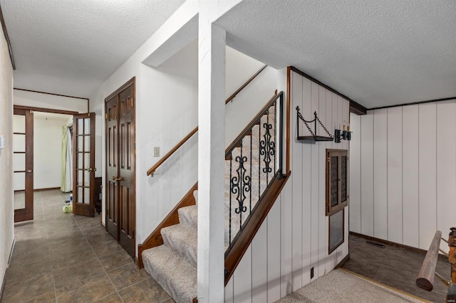 staircase with a textured ceiling, french doors, and wooden walls