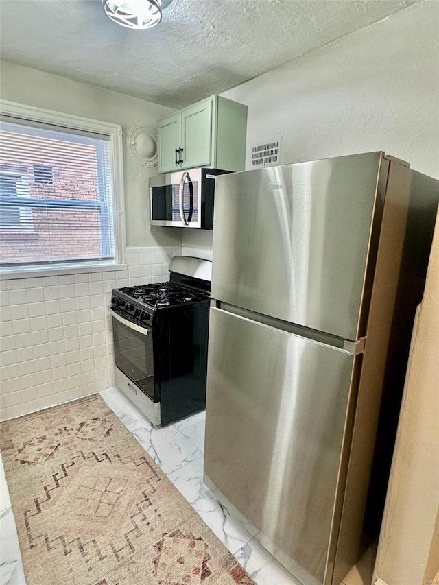 kitchen featuring tile walls, stainless steel appliances, a textured ceiling, and green cabinetry