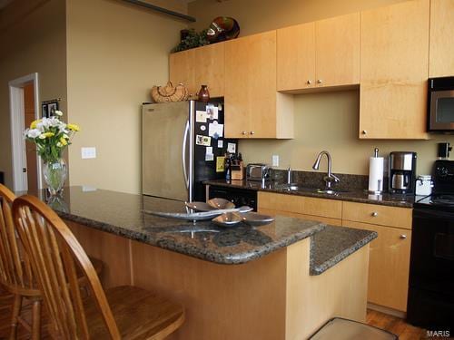 kitchen featuring sink, kitchen peninsula, dark stone counters, a breakfast bar, and appliances with stainless steel finishes