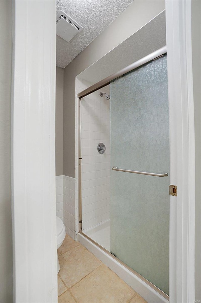 bathroom with toilet, walk in shower, tile patterned floors, and a textured ceiling