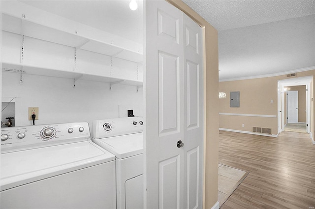 clothes washing area featuring a textured ceiling, electric panel, light hardwood / wood-style floors, washer and dryer, and ornamental molding