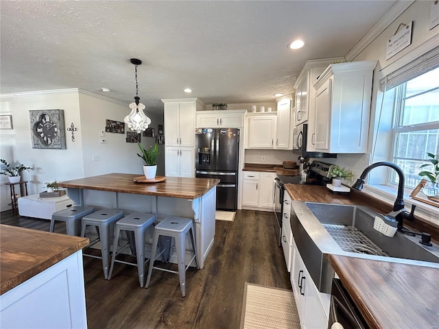 kitchen featuring butcher block counters, decorative light fixtures, a center island, black appliances, and white cabinets