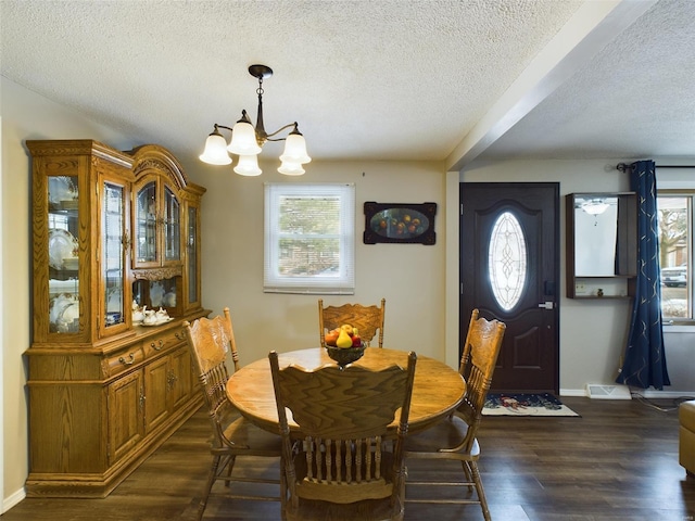 dining room featuring dark wood-type flooring, an inviting chandelier, and a textured ceiling