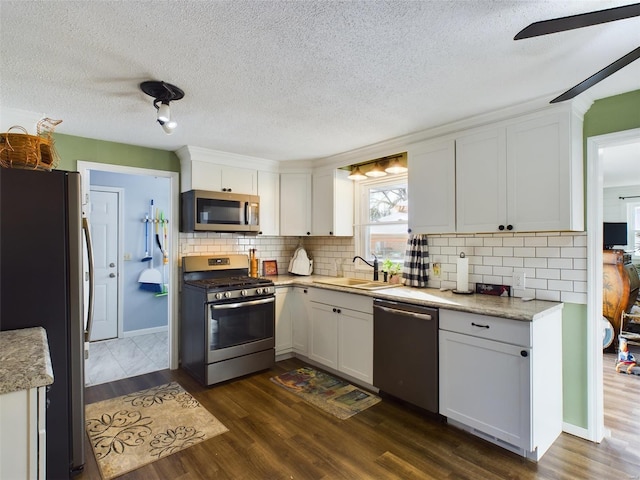 kitchen with white cabinets, appliances with stainless steel finishes, sink, backsplash, and dark hardwood / wood-style floors