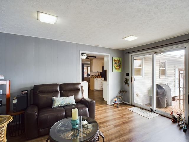 living room with a textured ceiling, light hardwood / wood-style flooring, and wooden walls