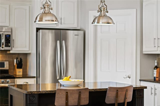 kitchen with decorative light fixtures, white cabinets, a center island, decorative backsplash, and appliances with stainless steel finishes