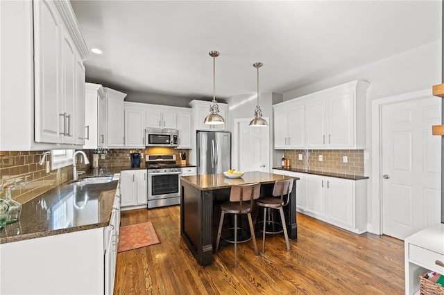 kitchen with dark wood-type flooring, a kitchen island, white cabinets, appliances with stainless steel finishes, and sink