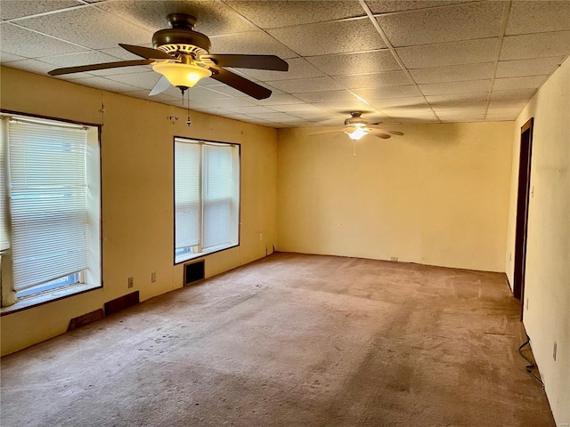 empty room with light colored carpet, a drop ceiling, and ceiling fan