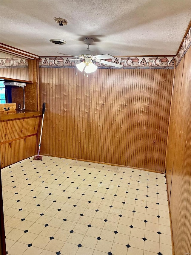 unfurnished dining area with a textured ceiling, ceiling fan, and wooden walls