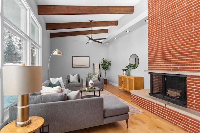 living room featuring wood-type flooring, a fireplace, ceiling fan, and beamed ceiling