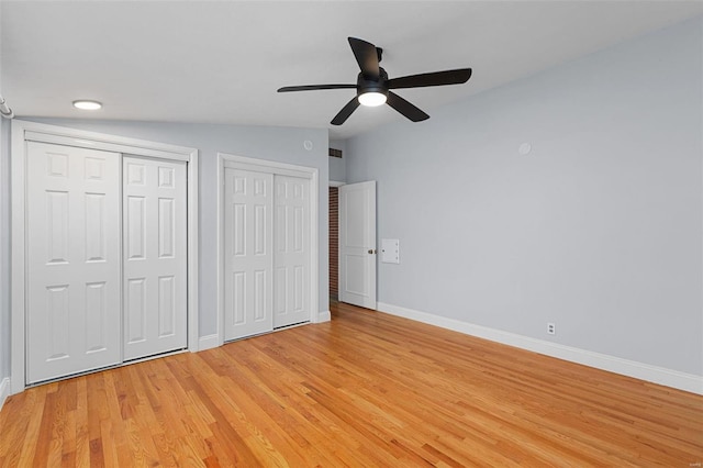 unfurnished bedroom featuring multiple closets, ceiling fan, vaulted ceiling, and light hardwood / wood-style flooring