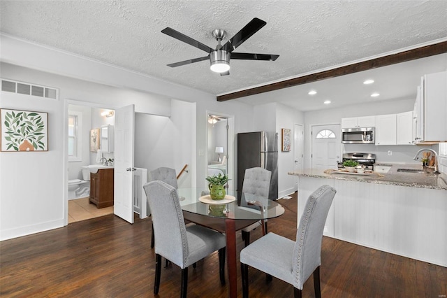 dining space featuring dark wood-type flooring, sink, a textured ceiling, and beamed ceiling