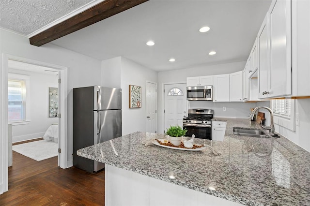 kitchen featuring appliances with stainless steel finishes, sink, white cabinets, light stone countertops, and beamed ceiling