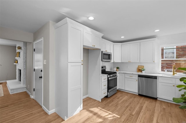 kitchen with light wood-type flooring, a brick fireplace, stainless steel appliances, and white cabinets