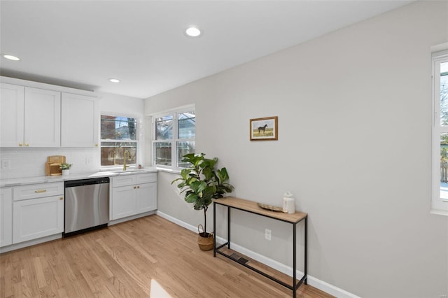 kitchen featuring decorative backsplash, white cabinets, stainless steel dishwasher, light hardwood / wood-style flooring, and sink