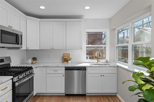 kitchen featuring light stone countertops, white cabinetry, stainless steel appliances, sink, and backsplash