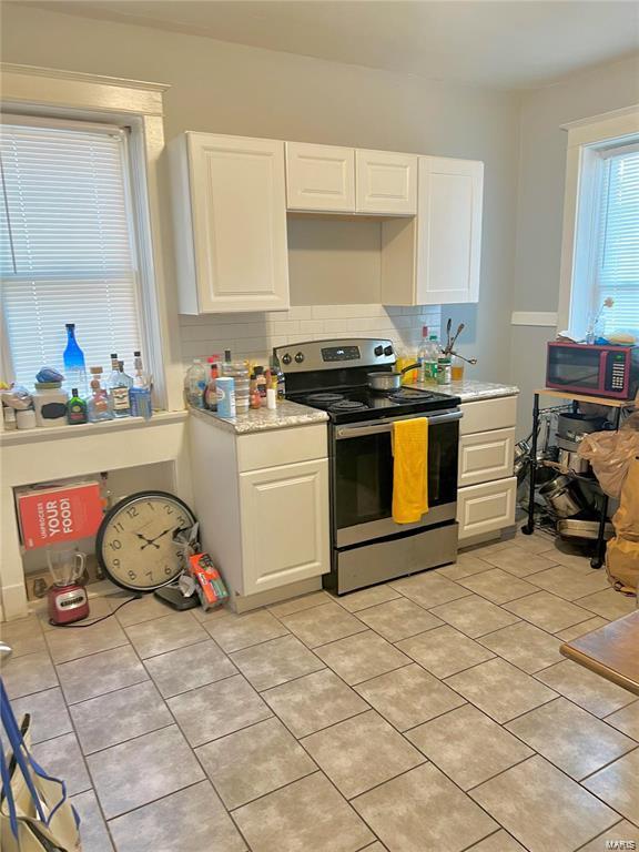 kitchen featuring tasteful backsplash, stainless steel electric range oven, white cabinets, and light tile patterned floors