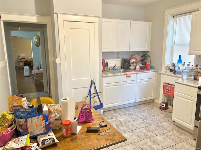 kitchen with white cabinetry, sink, light stone counters, backsplash, and light tile patterned flooring