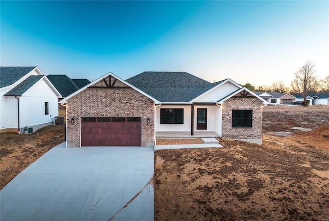 view of front of home featuring brick siding, roof with shingles, an attached garage, cooling unit, and driveway