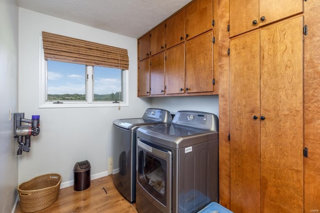 clothes washing area with washing machine and clothes dryer, light hardwood / wood-style flooring, cabinets, and a textured ceiling